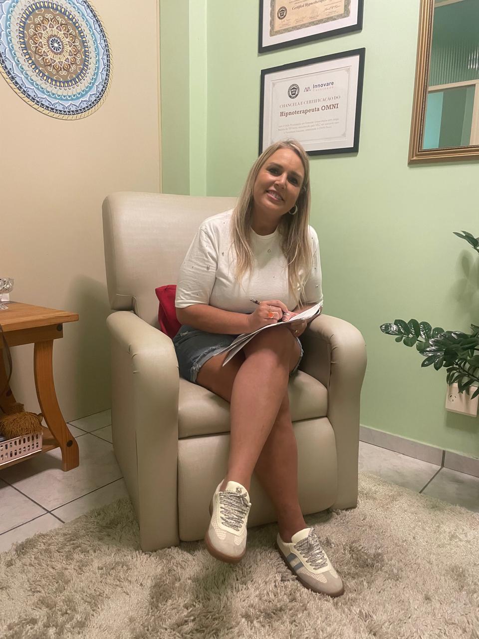 Simone no consultório, sentada em uma poltrona com um caderno nas mãos